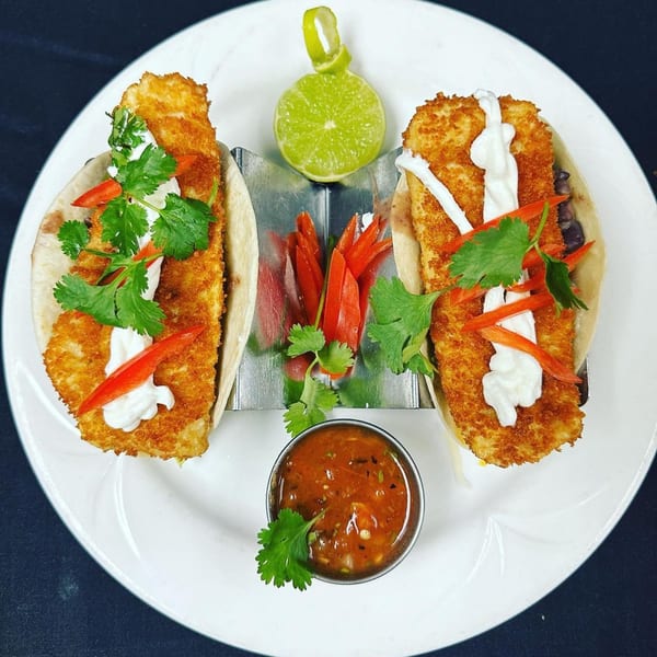 Two crispy fish tacos with cilantro, red peppers, and sour cream, served with salsa and lime.
