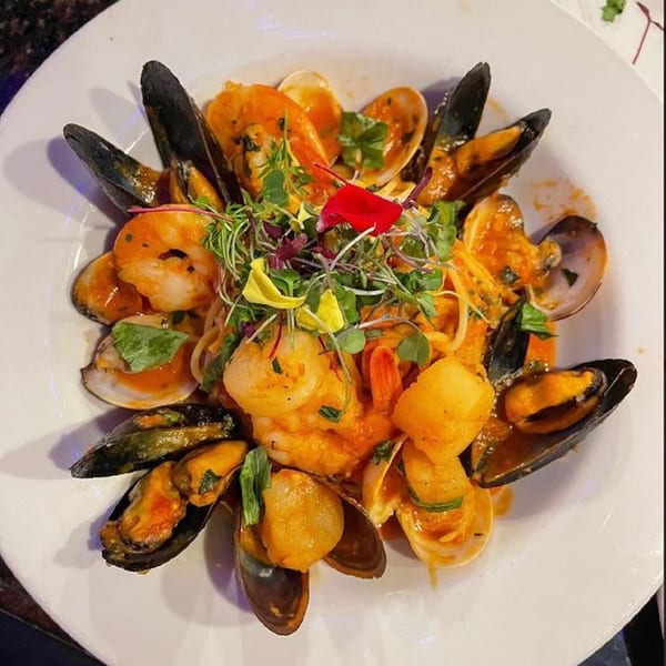 Seafood pasta with mussels, clams, shrimp, and scallops in a rich orange sauce, garnished with microgreens.