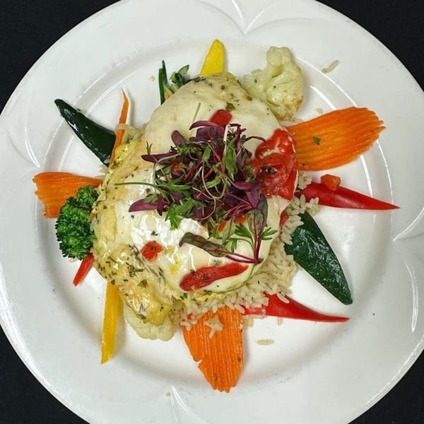 The Islander Grill's chicken dish with rice, colorful bell peppers, broccoli, and cauliflower on a white plate.