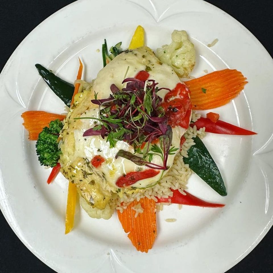 The Islander Grill's chicken dish with rice, colorful bell peppers, broccoli, and cauliflower on a white plate.